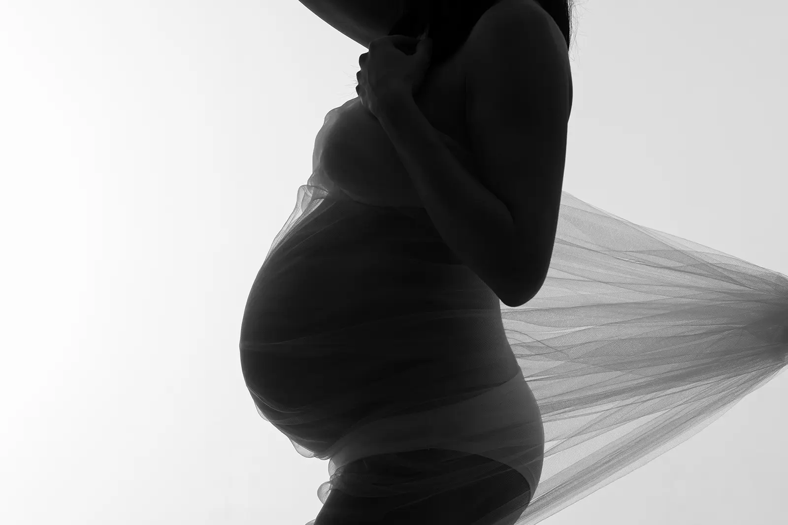 Silhouette di donna incinta avvolta nel tulle, scatto in controluce in bianco e nero nello studio a Milano