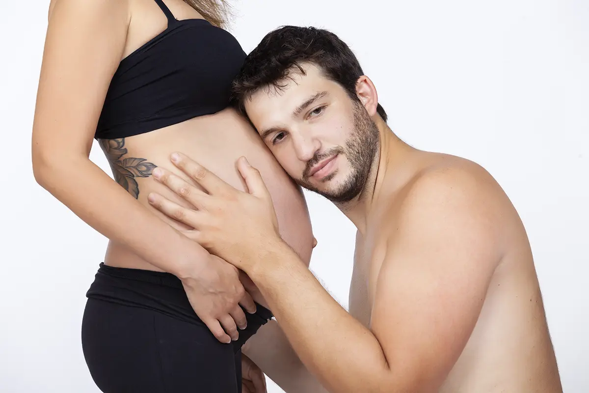Futuro papΓ che bacia il pancione della compagna durante un book fotografico gravidanza in studio a Milano
