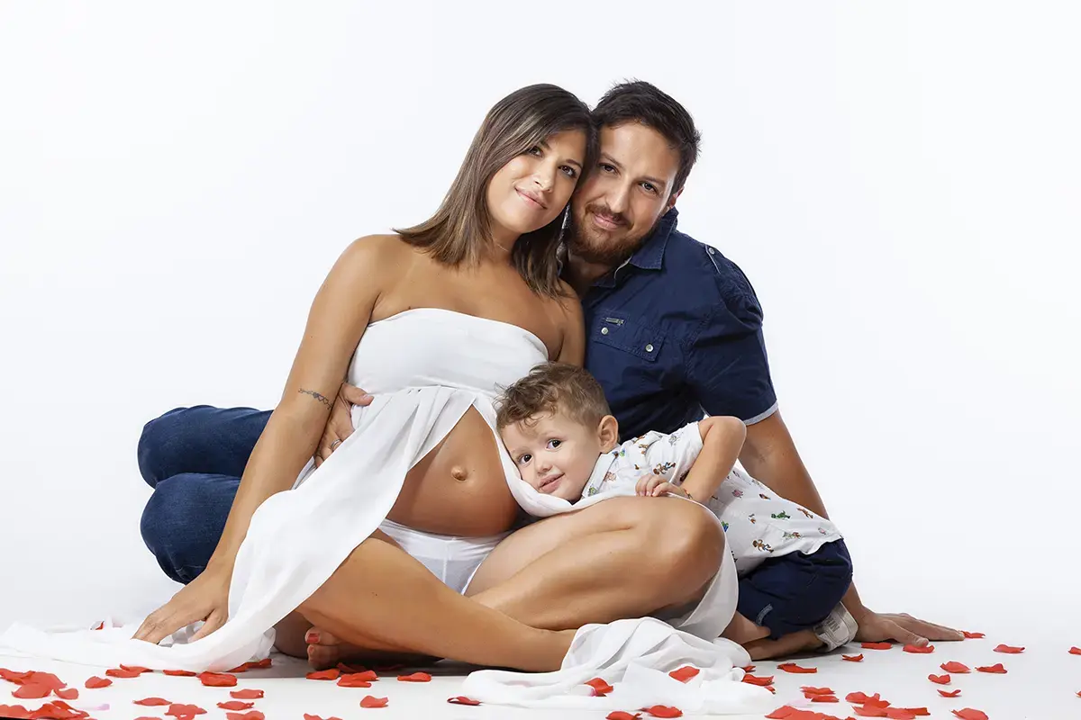 Famiglia in attesa seduta tra i petali rossi col fratellino, servizio fotografico gravidanza in studio a Milano