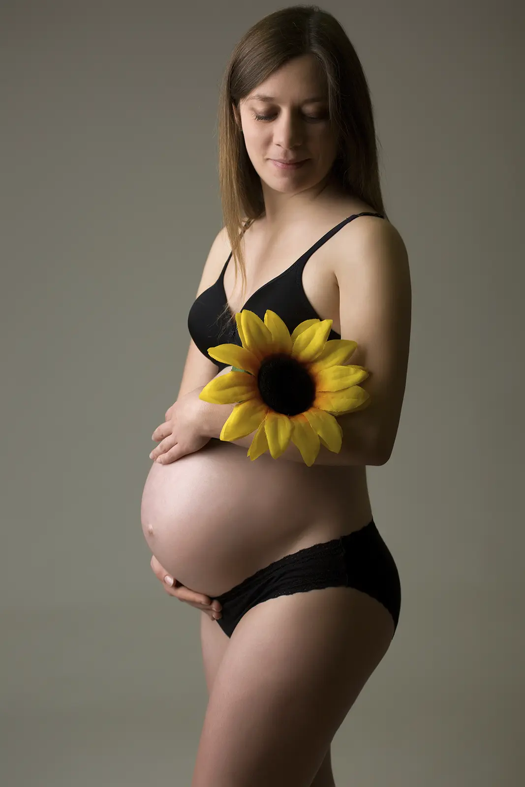 Futura mamma con girasole tra le mani su fondo grigio, book fotografico gravidanza in studio a Milano