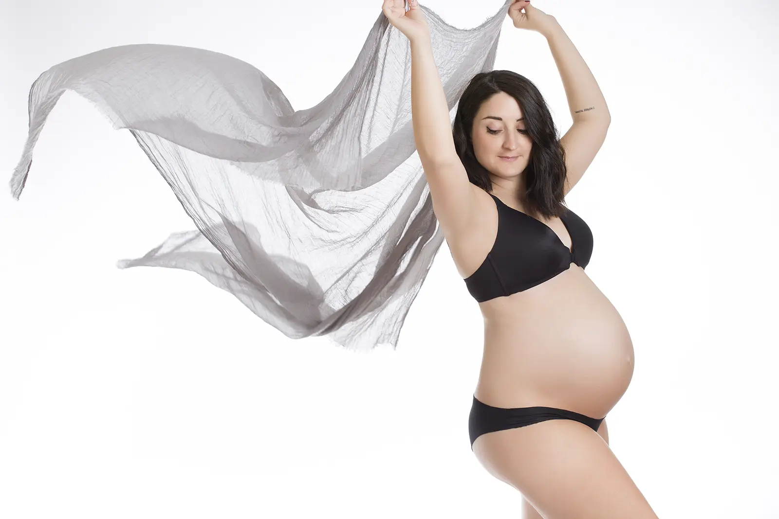 Futura mamma con velo grigio in movimento durante un book fotografico gravidanza in studio a Milano