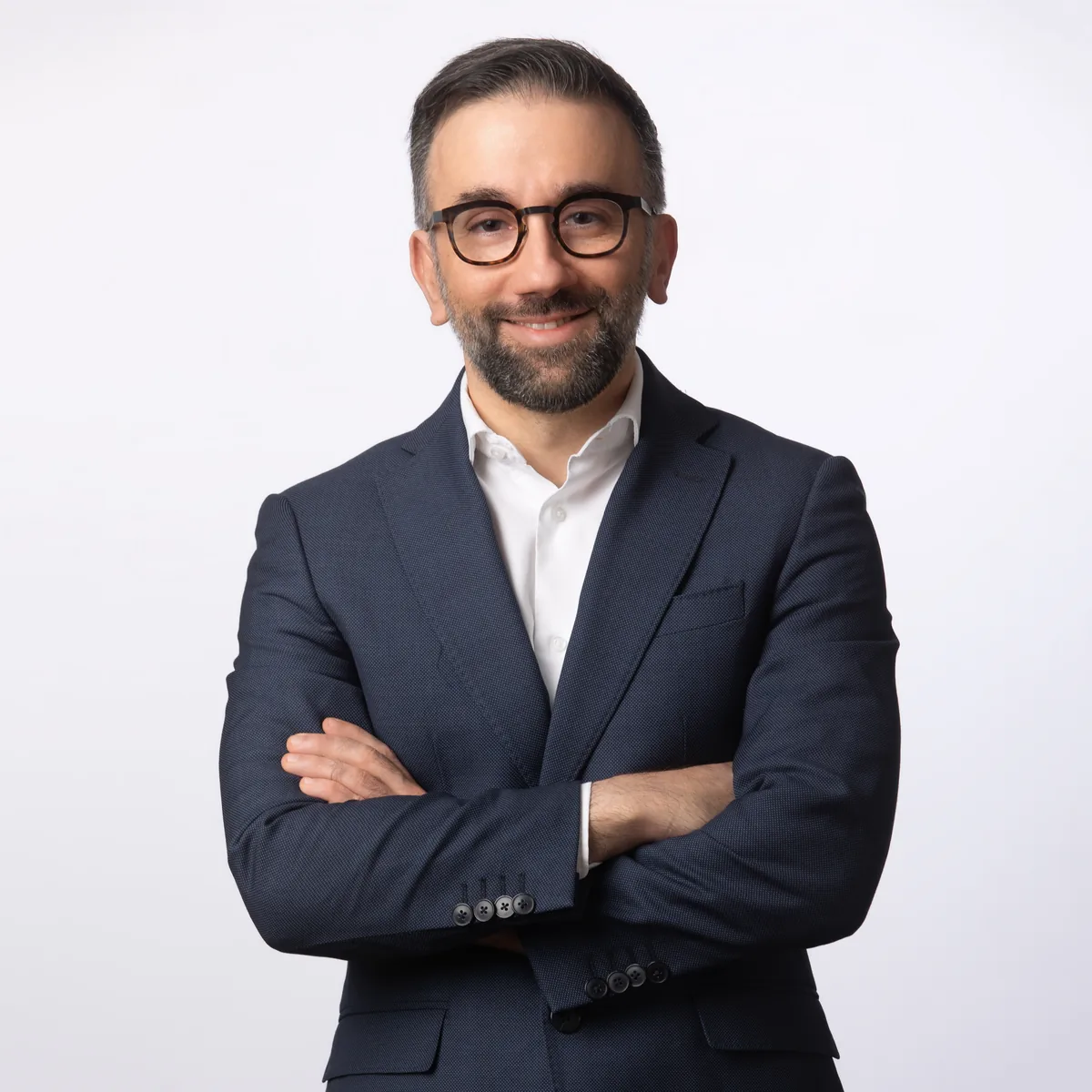 Foto profilo LinkedIn di un uomo con occhiali e barba in abito blu, ritratto in studio a Milano